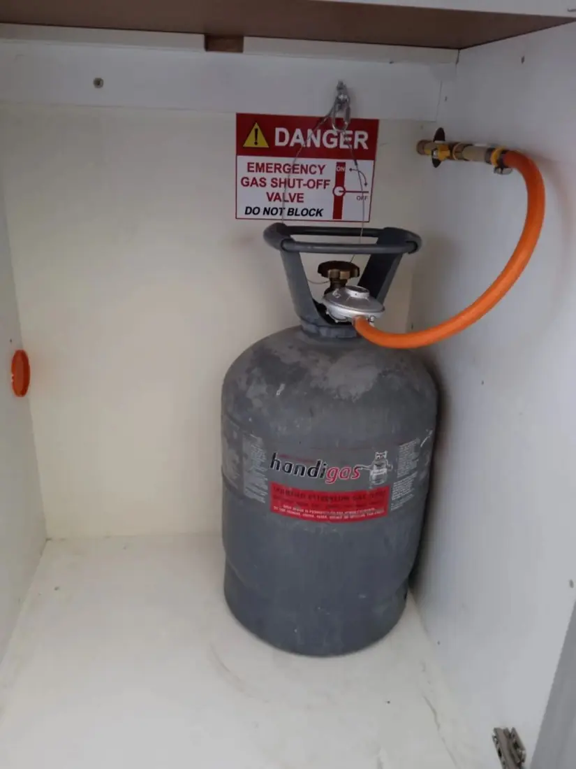 A gas cylinder in a kitchen cabinet with an emergency shut-off sign