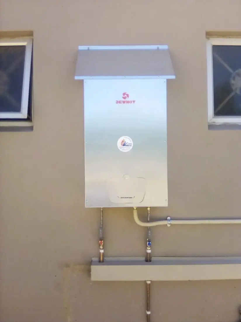 A Dewhot gas geyser in a stainless steel cover, installed on an outside wall by WF Gas