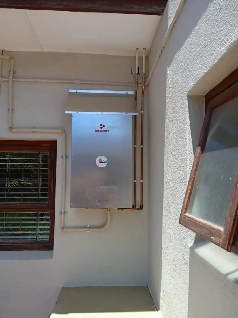 A gas geyser in a stainless cover beside a window
