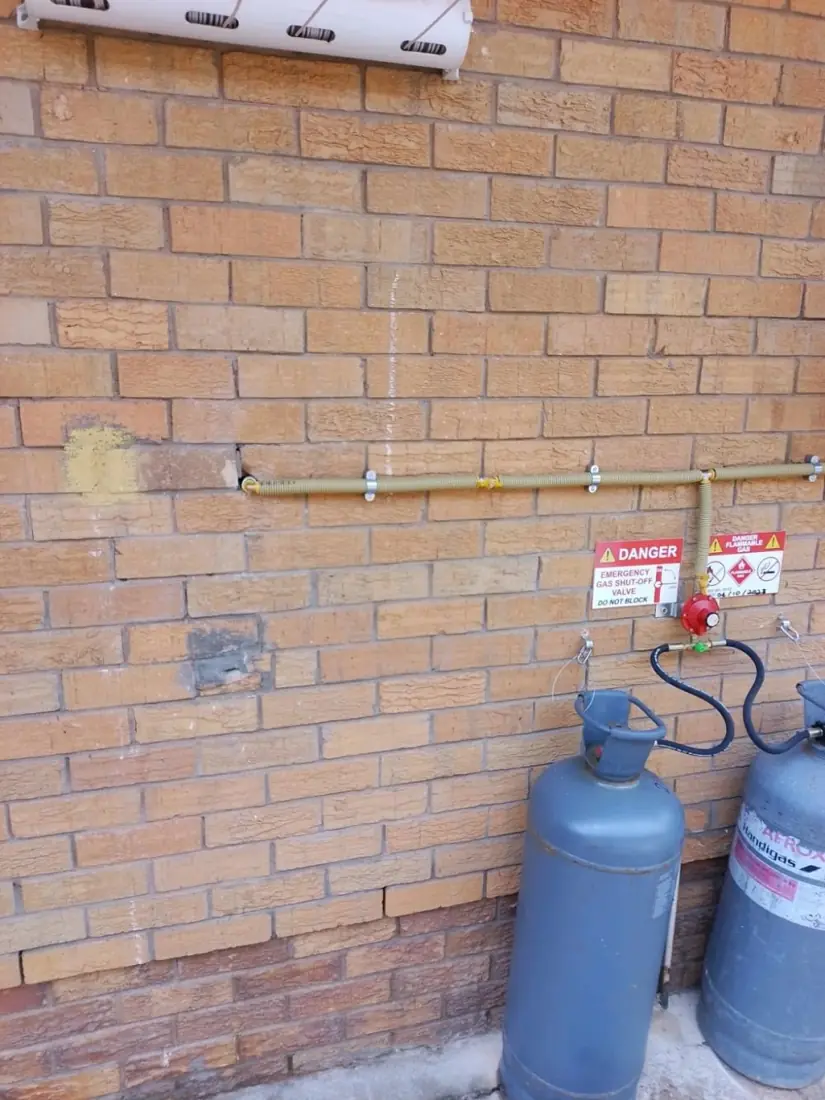 Twin LPG cylinders with a changeover regulator against a brick wall